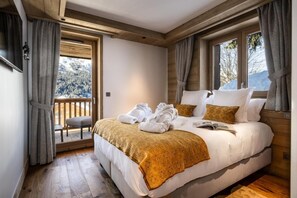 A bedroom with a large bed, a wooden ceiling, and a view of a snowy landscape through a window. - Wifi, 150m from ski slopes, 1st floor, view mountain, sauna, hammam, balcony, fireplace or stove, tv (Méribel - Les Allues)