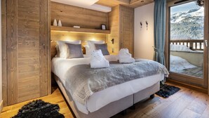 A bedroom with a large bed, wooden paneling, a view of a snowy landscape through a sliding door, and a small shelf with decorative items. - Wifi, 150m from ski slopes, 1st floor, view mountain, sauna, hammam, balcony, fireplace or stove, tv (Méribel - Les Allues)