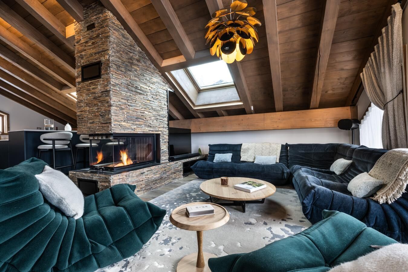 Un salon chaleureux avec une cheminée en pierre, des canapés sombres et une table basse ronde en bois.