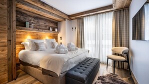 Un dormitorio moderno con cabecera de madera, una cama grande con ropa de cama blanca, un banco tapizado en gris y una silla.