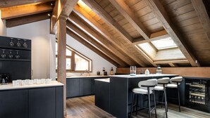 Una cocina moderna con armarios oscuros, una isla central con taburetes de bar y un tragaluz.