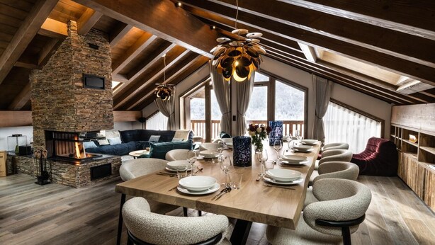 Un comedor con chimenea de piedra, vigas de madera en el techo y un ventanal grande.
