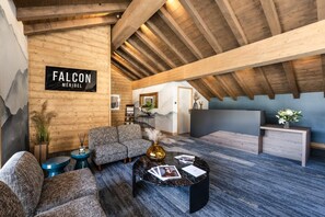 A spacious living area with a high ceiling and wooden beams, featuring a sofa set, a coffee table, and a reception desk. - Wifi, Ground floor, view mountain, sauna, hammam, terrace, fireplace or stove, tv, 85m², Méribel (Méribel - Les Allues)