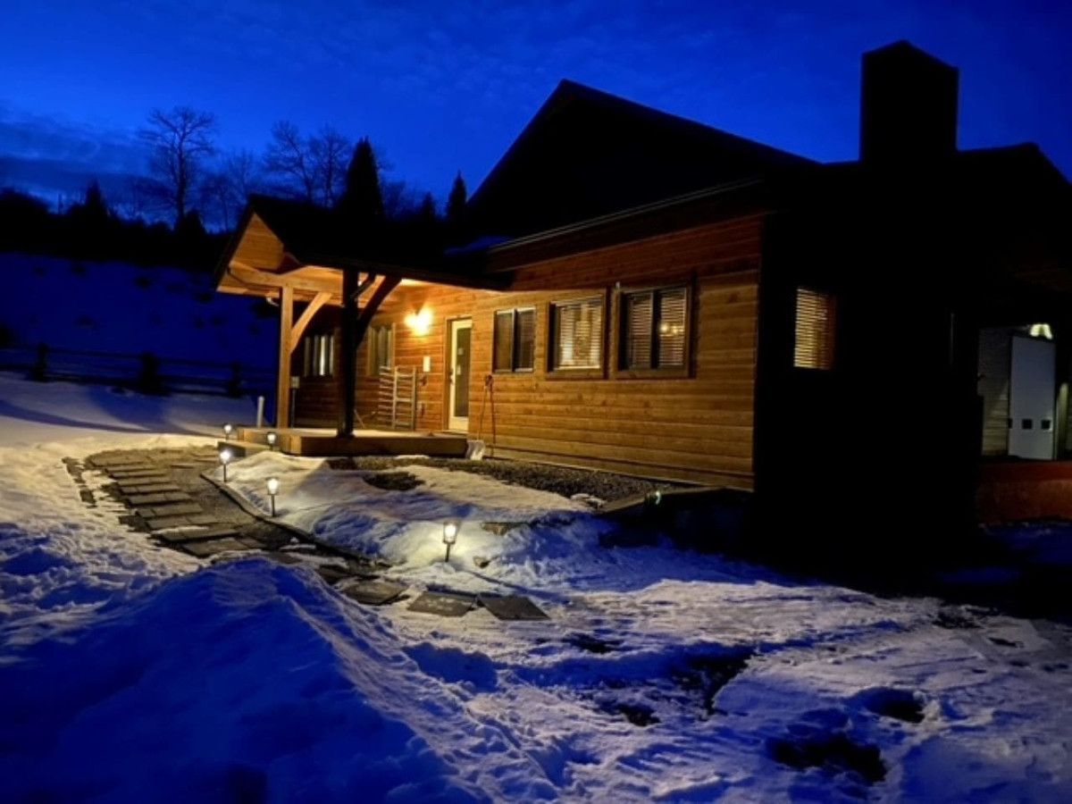 A wooden cabin with a covered porch and a snow-covered driveway at night.