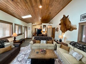 A cozy living room with a wooden ceiling, two sofas, a coffee table, and a large animal hide on the wall.