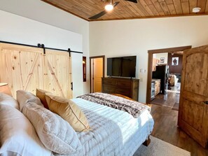 A bedroom with a bed, pillows, a wooden headboard, a television, and a wooden wardrobe.
