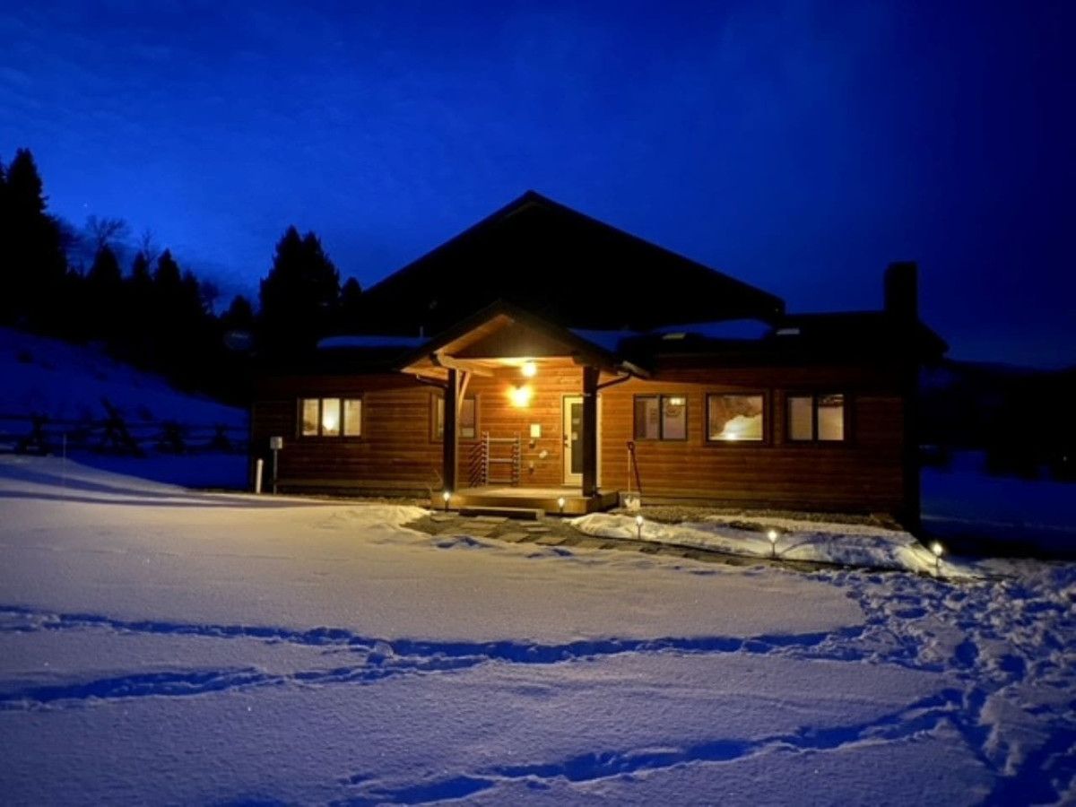 A wooden cabin with a sloped roof, a front porch, and a lit entrance.