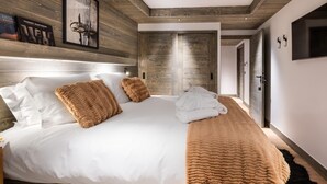 A modern bedroom with a large bed, wooden paneling on the walls, a mounted TV, and a framed picture. - Wifi, 150m from ski slopes, Ground floor, sauna, hammam, terrace, fireplace or stove, tv, 84m² (Méribel - Les Allues)