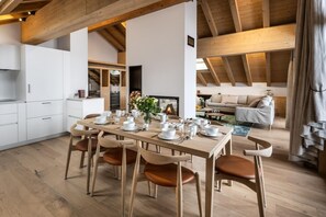 Een moderne keuken met witte kasten, een houten eettafel gedekt voor vier personen, en een open haard op de achtergrond.