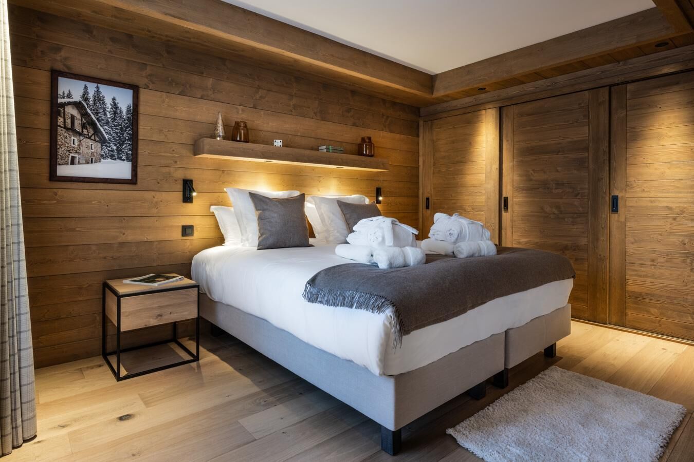 Une chambre à coucher moderne avec un mur décoré de panneaux en bois, un grand lit avec de nombreux coussins, une table de chevet et une commode.