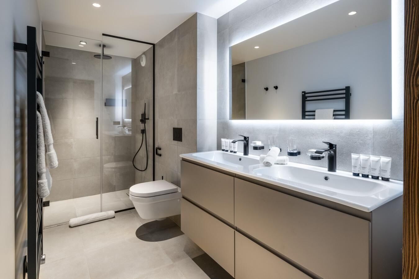 Une salle de bain moderne avec une douche à l’italienne en verre, des toilettes, un meuble-lavabo double et un grand miroir.