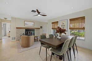 A dining area with a wooden table, cushioned chairs, a fireplace, and a ceiling fan.