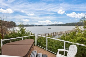 A deck with a view of a lake, a wooden deck, and a white chair. - Beach Front Retreat :Private Beach and Dock Access, Hot Tub, BBQ &Free Kayaks! (Sooke)