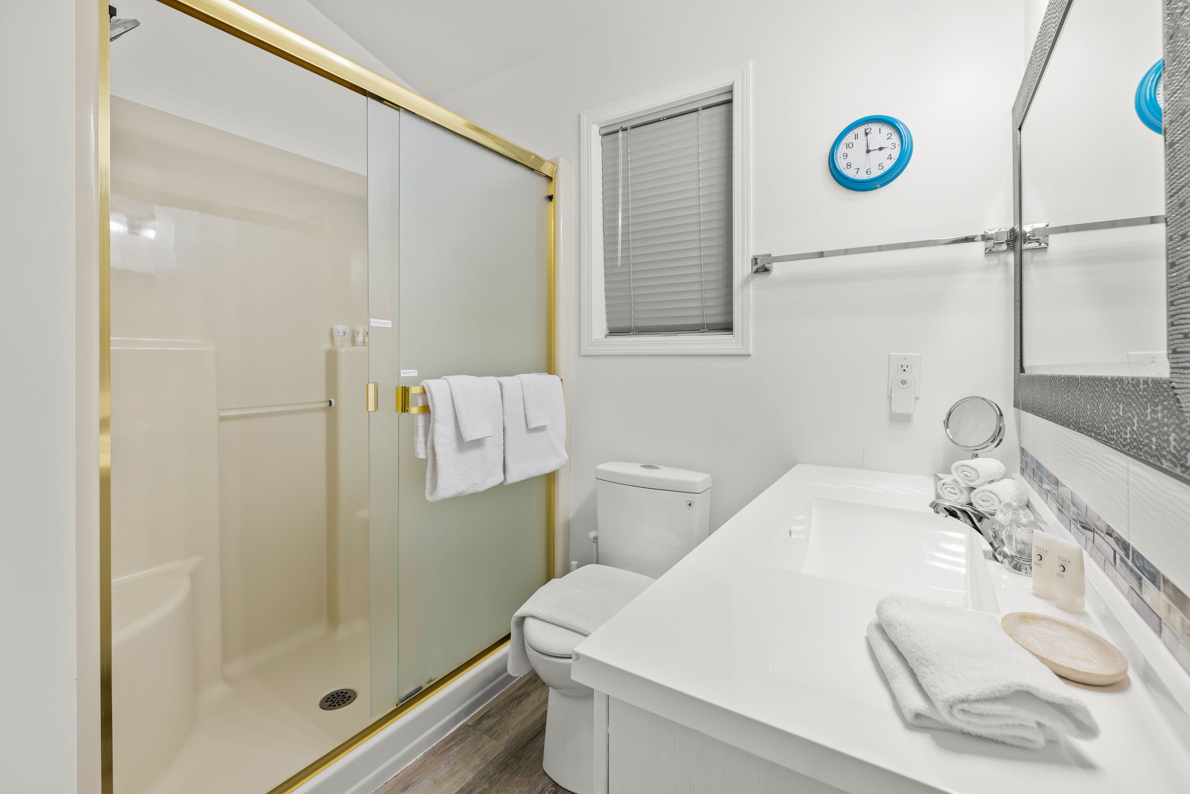 Et moderne badeværelse med en glasafskærmet bruseniche, et hvidt toilet, et badekar og en vask med spejl og håndklæderække.