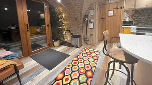 A cozy kitchen with a brick ceiling, wooden cabinets, and a colorful hexagonal rug. - Honeybee Home -  a hobbit hut that sleeps 4 guests  in 2 bedrooms (Llansantffraid)
