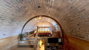 A cozy interior with a brick archway leading to a bedroom. A staircase with wooden railings and a colorful cushion is visible. - Honeybee Home -  a hobbit hut that sleeps 4 guests  in 2 bedrooms (Llansantffraid)