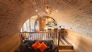 A cozy interior with a brick ceiling, a wooden staircase, a dining area, and a sofa with orange cushions. - Honeybee Home -  a hobbit hut that sleeps 4 guests  in 2 bedrooms (Llansantffraid)