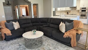 A modern living room with a sectional sofa, a round coffee table, and a kitchen in the background. - Charming spacious 4 Bed house with WiFi and AC large backyard and pool. (Bakersfield)