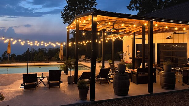 Un espace extérieur aménagé en terrasse, avec une piscine, des chaises longues et des guirlandes lumineuses.