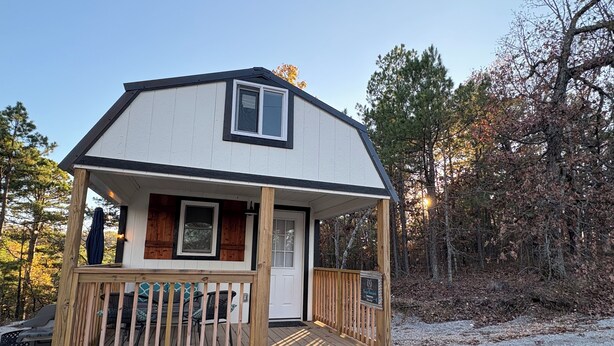 Une petite cabane avec une terrasse en bois, un porche et une porte d’entrée.