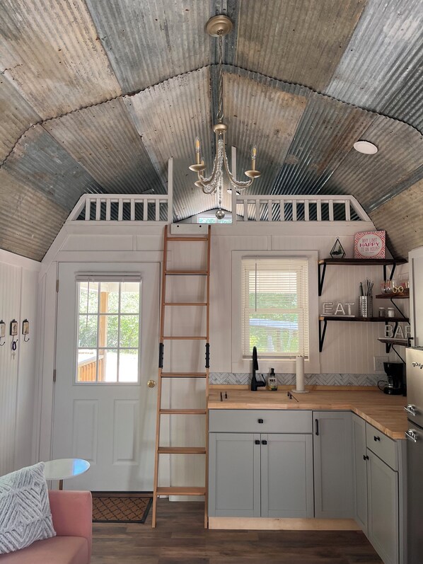 A rustic kitchen with a wooden ladder, a chandelier, and a window with blinds. - Bougie Boondock Tiny Home (Eureka Springs)