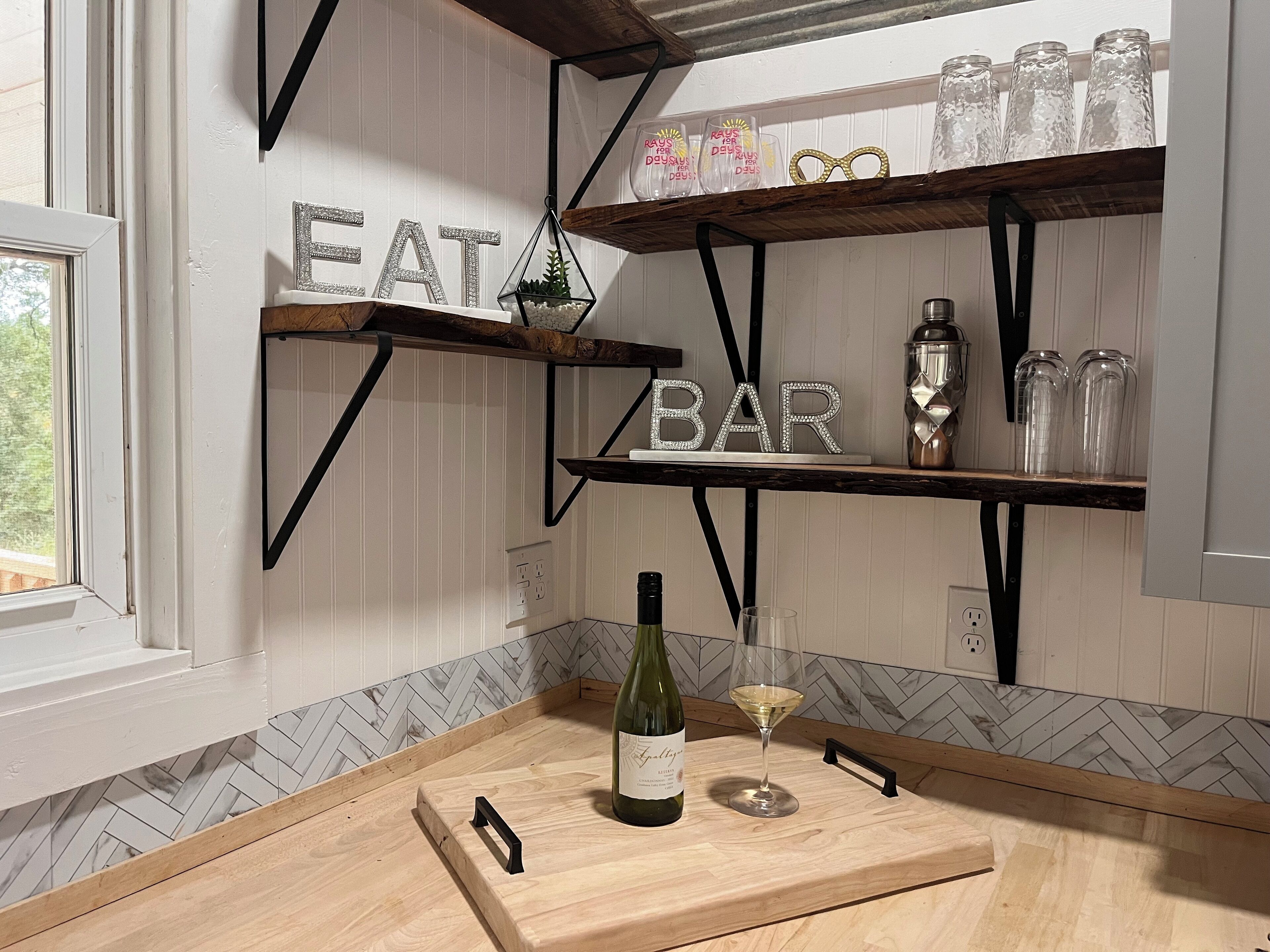 Una cucina con mensole di legno etichettate 'EAT' e 'BAR', una bottiglia di vino e un bicchiere su un piano di lavoro in legno.