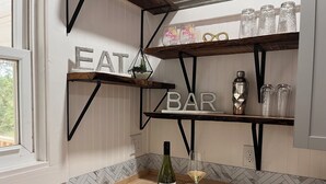 Une cuisine avec des étagères en bois portant les inscriptions « À MANGER » et « BAR », une bouteille de vin et un verre posés sur un comptoir en bois.