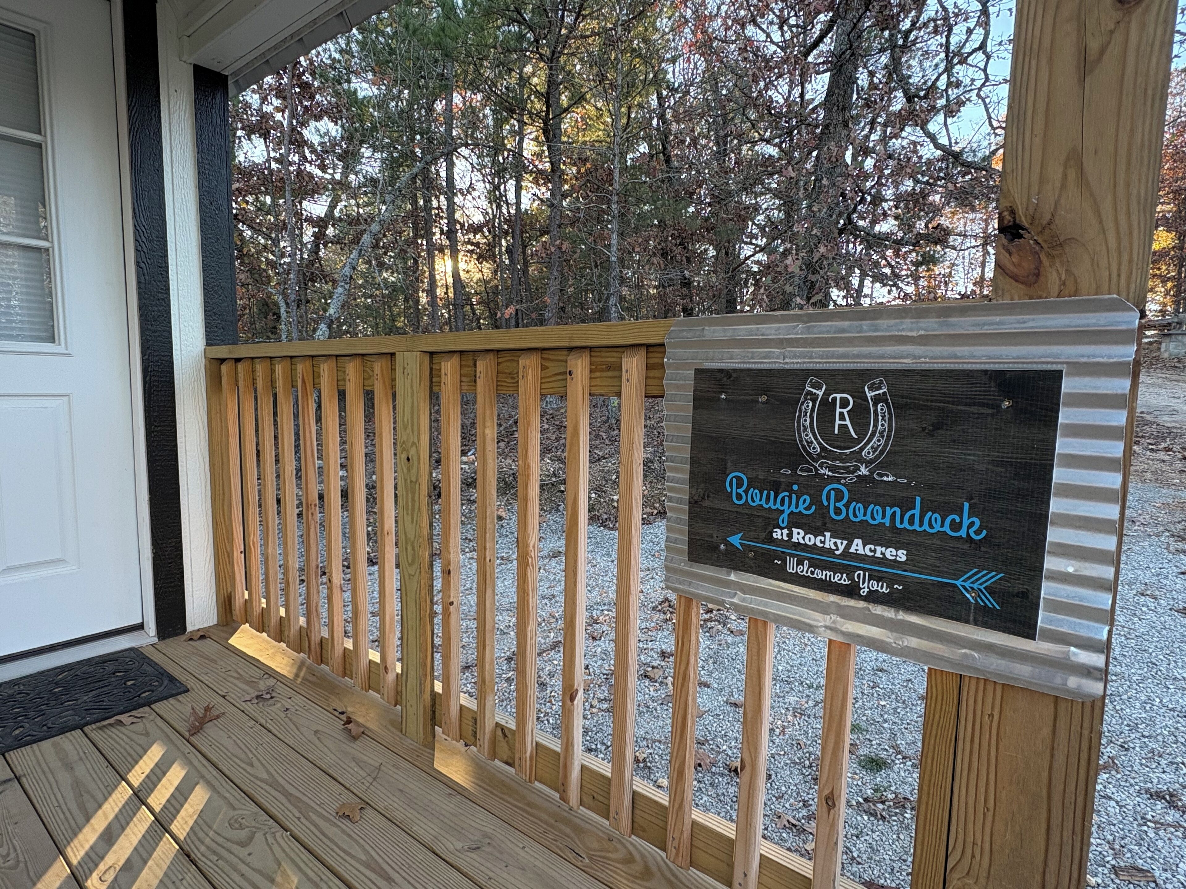 A wooden deck with a sign for 'Boujie Boondock at Rocky Acres' welcoming visitors.