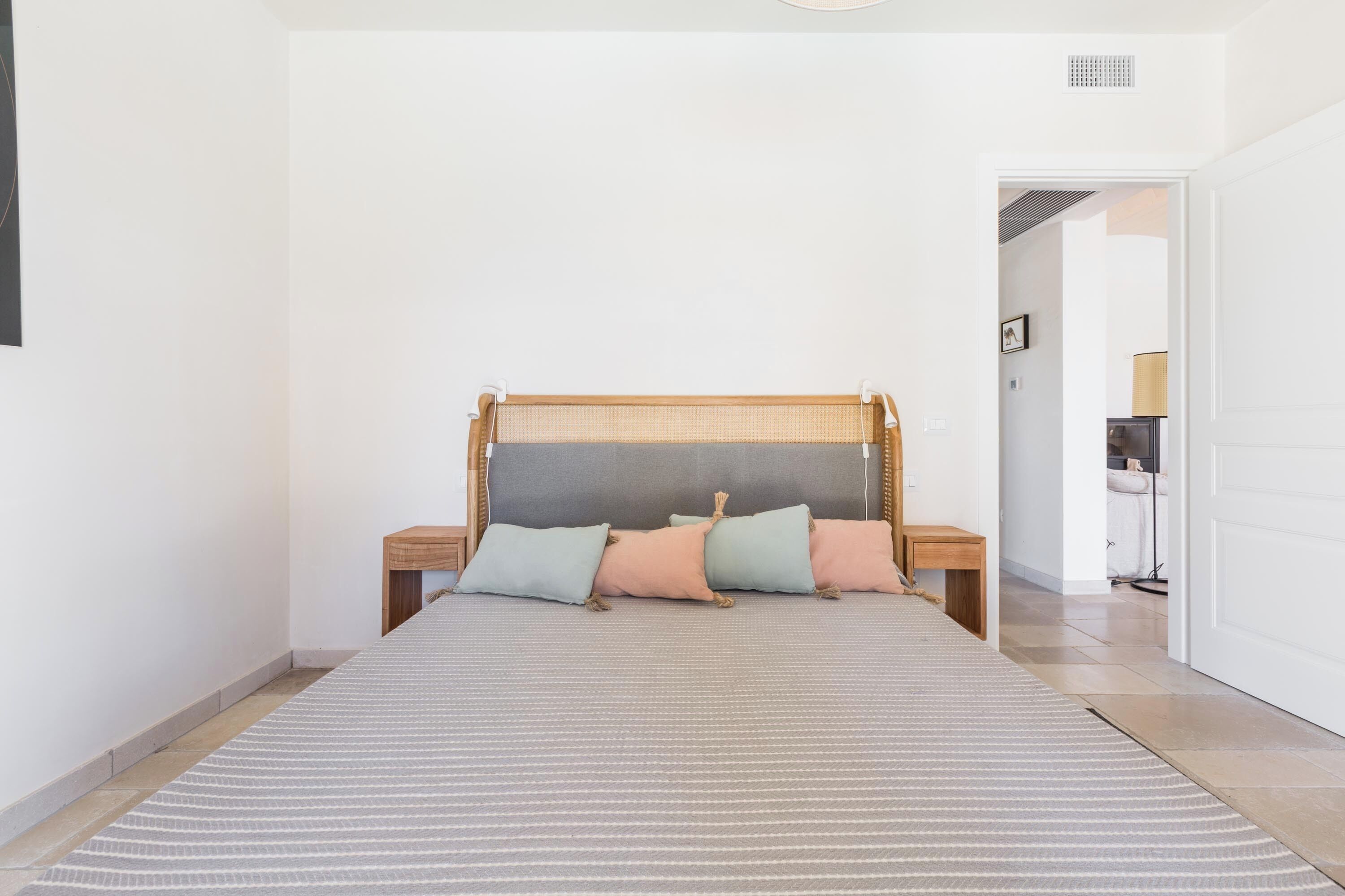 Un dormitorio con cama, almohadas, mesita de noche y una puerta que da a otra habitación.