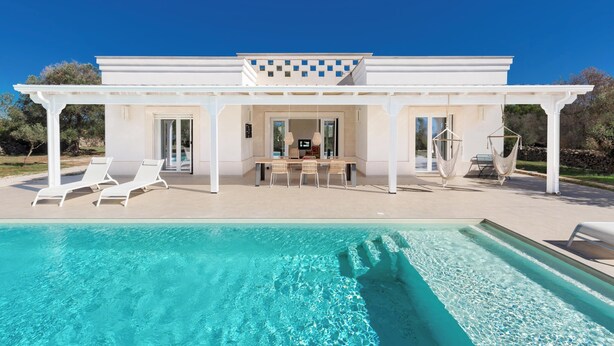 Een modern huis met zwembad, terras en een pergola.