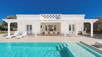 Een modern huis met zwembad, terras en een pergola.
