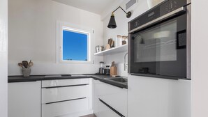 Een moderne keuken met witte kasten, een zwart aanrecht, een raam met uitzicht op blauwe lucht en een inbouwoven.