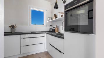 Een moderne keuken met witte kasten, een zwart aanrecht, een raam met uitzicht op blauwe lucht en een inbouwoven.