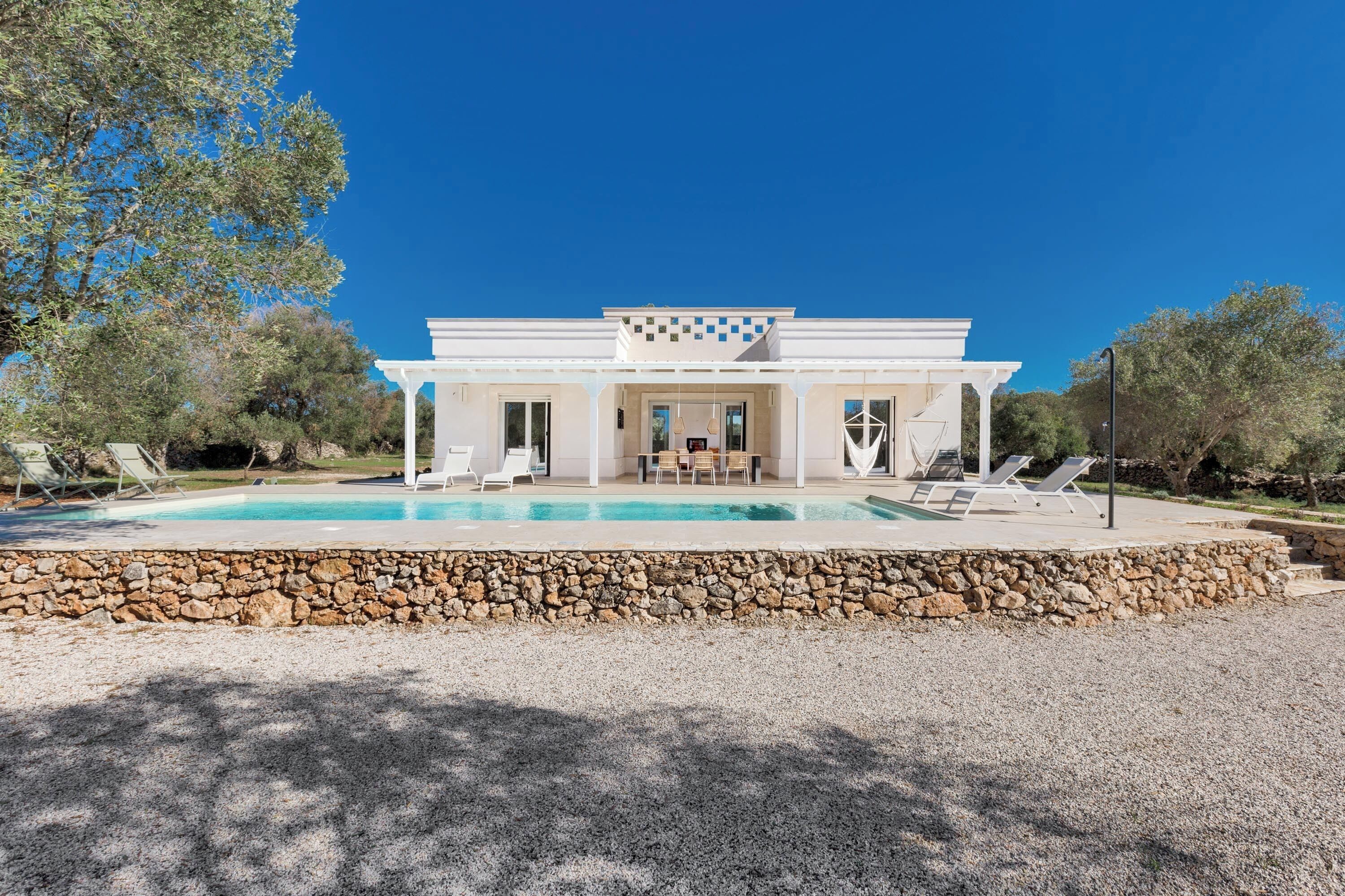 Une villa moderne dotée d’une piscine, d’un espace extérieur aménagé et d’un mur en pierre qui entoure la zone de la piscine.