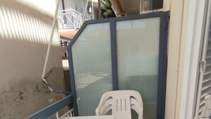 Un pequeño balcón con una mesa blanca, una silla de plástico y dos sillas de metal, además de una parrilla metálica.