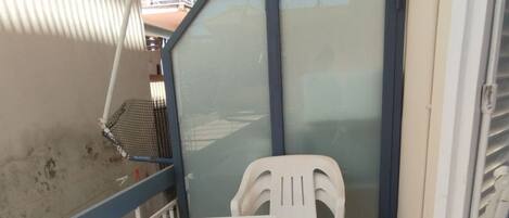 A small balcony with a white table and a plastic chair, a metal chair, and a metal grill.