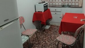 Una cocina compacta con refrigerador, una mesa con sillas y un ventanal con cortinas rojas.