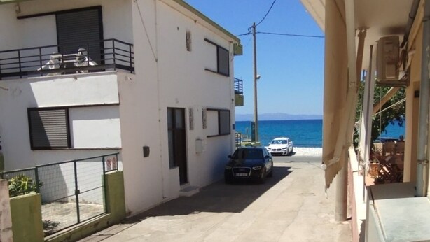 Una calle estrecha con un edificio a la izquierda y vistas al mar a la derecha. Hay dos coches aparcados a lo largo de la calle.