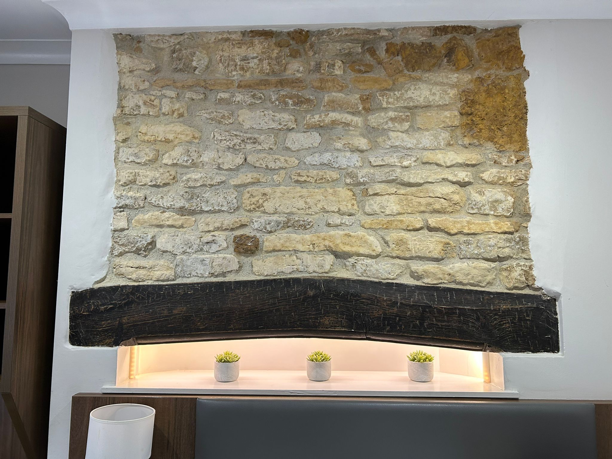 A stone fireplace with a dark wood mantel and three small potted plants.