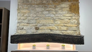 A stone fireplace with a dark wood mantel and three small potted plants.