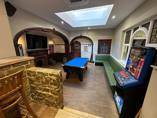 Une salle de billard équipée d’une table de billard, d’un canapé vert, d’un coin bar et d’un appareil à sous.