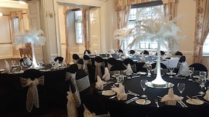 Une salle à manger élégante, avec des tables rondes dressées pour le repas, chacune recouverte d’une nappe noire et agrémentée de serviettes blanches.