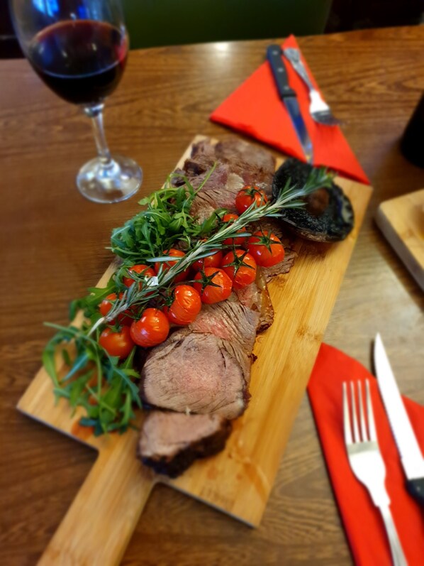 A wooden cutting board with sliced meat, cherry tomatoes, and herbs. - The Hind Hotel (Wellingborough)