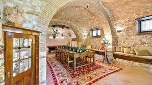 Un intérieur rustique avec des murs en briques apparentes, une table à manger en bois avec des chaises, un canapé et un lustre décoratif.