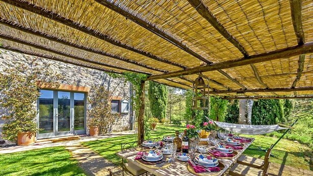 Un espace de restauration en plein air avec une longue table dressée pour un repas, entouré de murs en pierre et de verdure.