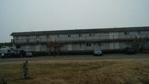 A multi-story motel with a central staircase, parking lot, and a grassy area in front. - Soothing 2-bdrm condo near beach with WiFi and Fireplace (Ocean Shores)