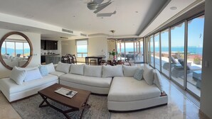 A spacious living room with a large sectional sofa, a coffee table, and a view of the ocean through large windows. - Penthouse Luxury. WOW! Panoramic views of everything! BradAndJoeyRentals (Nuevo Vallarta)