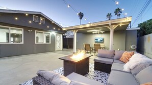 Eine Terrasse im Freien mit Feuerstelle, Sitzgelegenheiten und einem Fernseher.