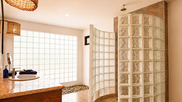 Une salle de bain dotée d’une douche à parois de verre, d’un lavabo avec un miroir et d’une fenêtre laissant entrer la lumière naturelle.