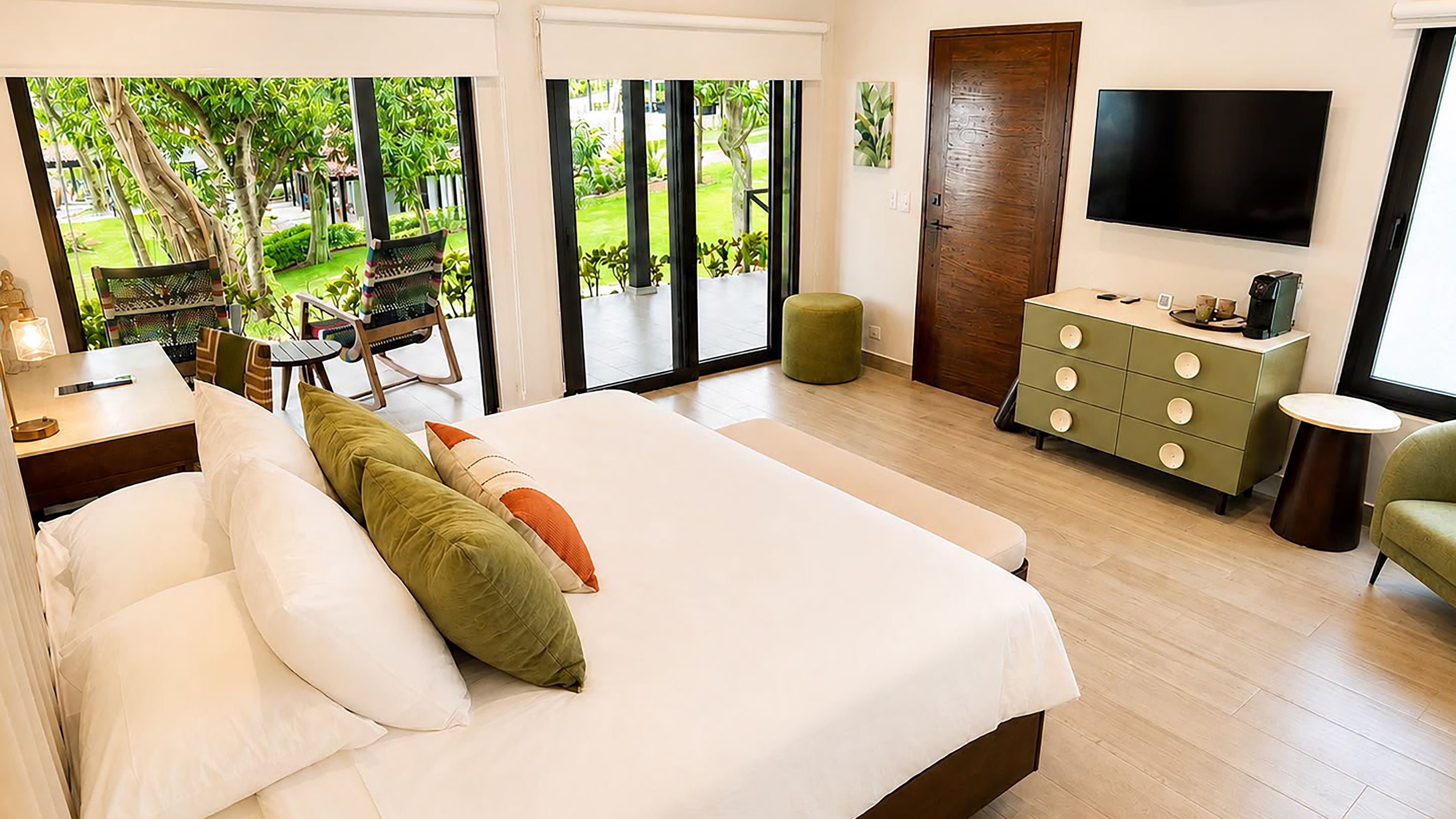 A bedroom with a large bed, a dresser, a television, and a view of a garden.